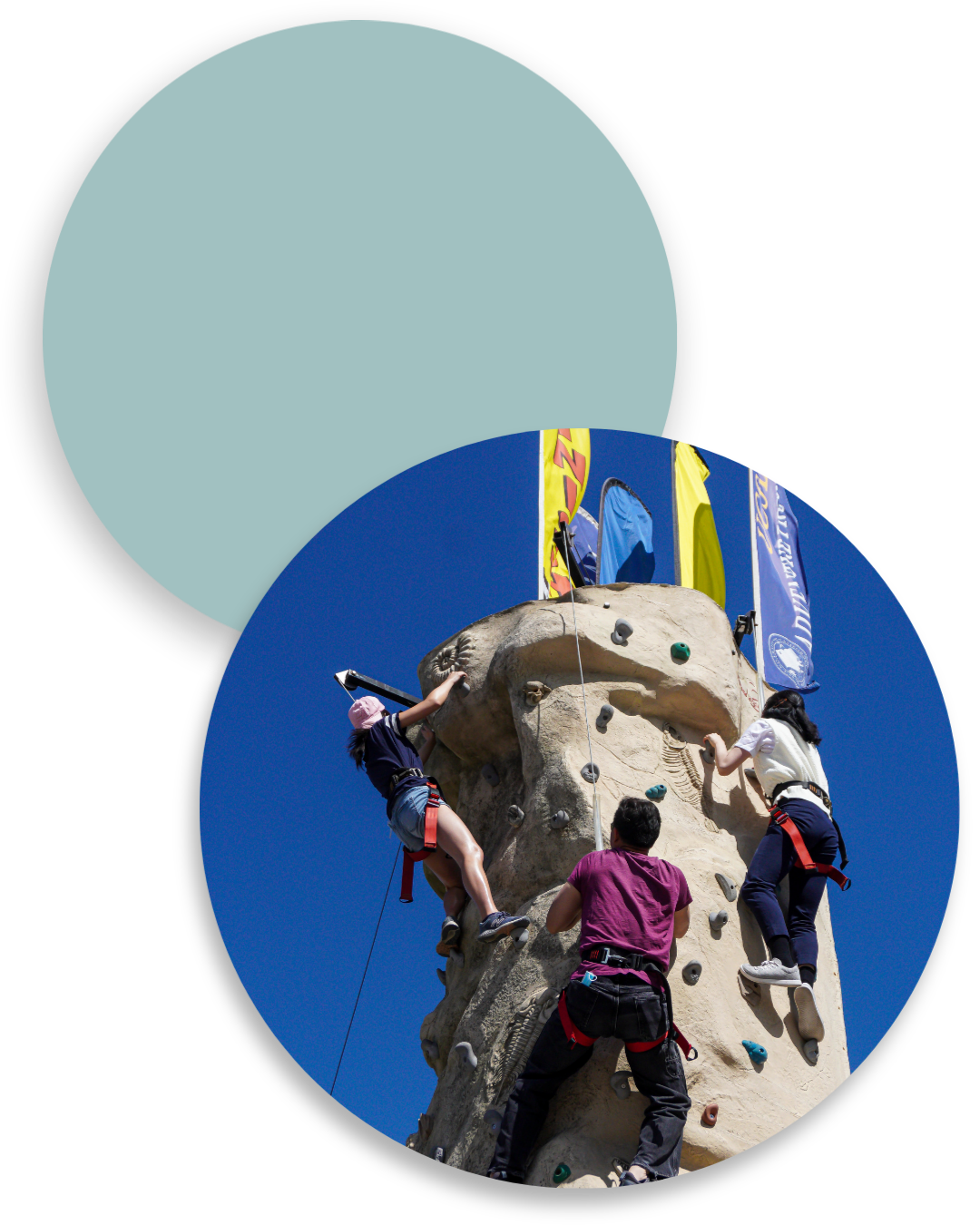 Three people climb a portable rock wall under a clear blue sky at an outdoor campus event.